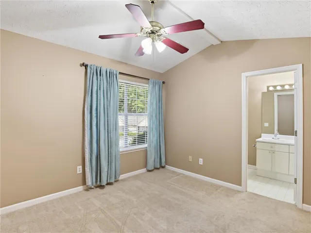 This airy bedroom features a vaulted ceiling, soft carpeting, and a private en suite.