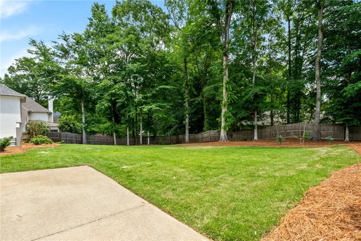 This spacious yard offers a serene retreat with mature trees and a fenced perimeter.