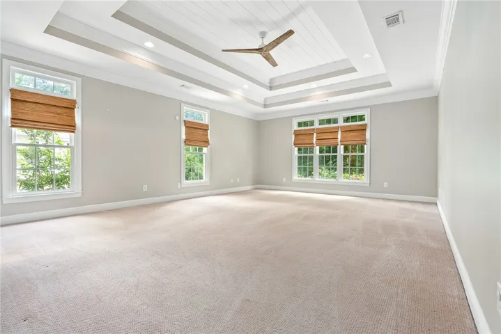 This spacious bedroom features a beautiful tray ceiling, recessed lighting, and ample natural light.