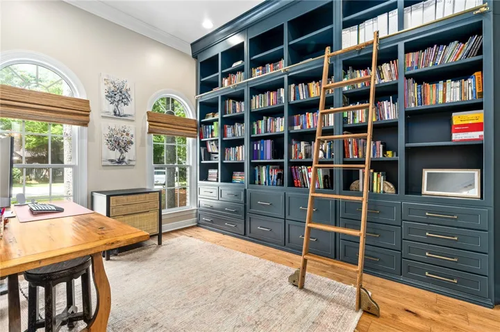 This elegant library office features extensive built-in shelving, high ceilings, and beautiful hardwood floors.