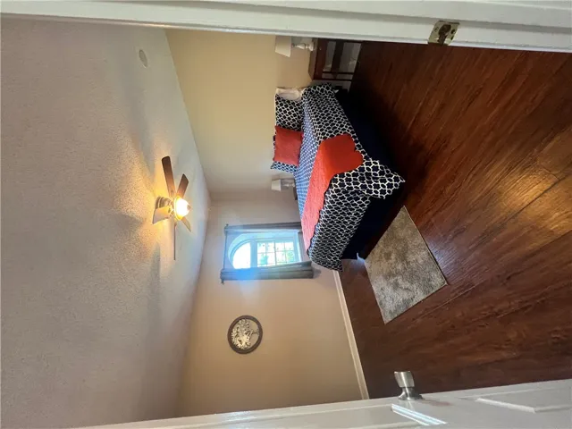 This cozy bedroom features warm wood flooring and a charming arched window, creating an inviting retreat.