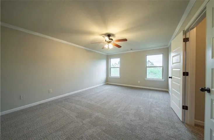 This spacious bedroom offers comfortable carpeting and elegant crown molding, perfect for peaceful living.
