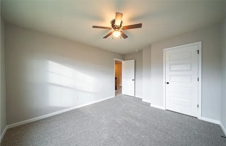 This airy bedroom features plush carpeting and a modern ceiling fan, creating a comfortable living space.