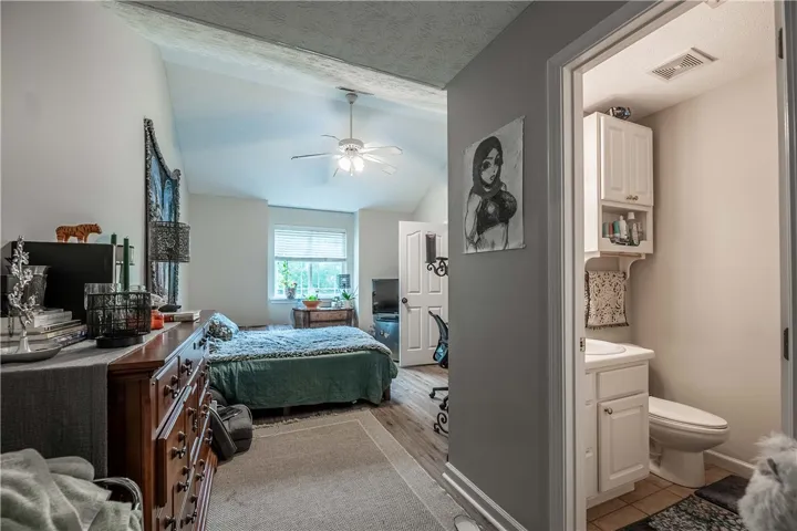 A naturally illuminated bedroom offers vaulted ceilings and wood flooring with an adjacent bathroom.