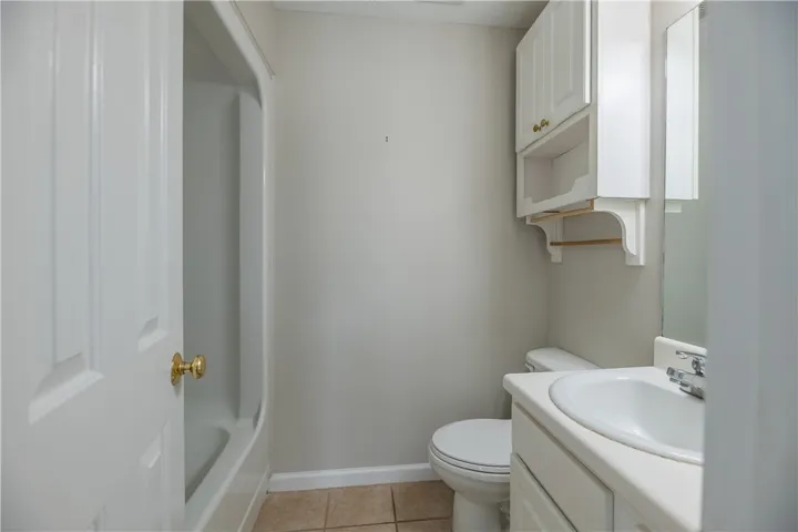 A compact full bathroom featuring a tub and shower combination with an overhead storage cabinet.