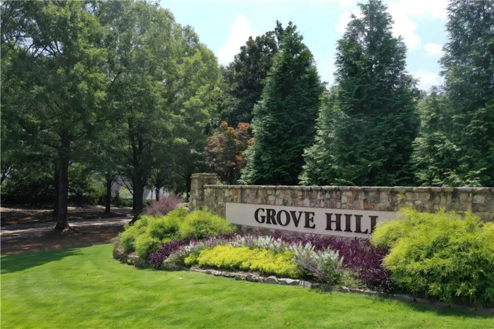 Grove Hill welcomes with a stone entrance, vibrant landscaping, and mature trees.