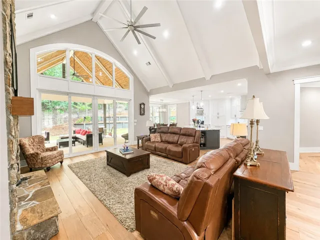 An airy living area boasts vaulted ceilings and hardwood flooring, flowing seamlessly to an outdoor living space.