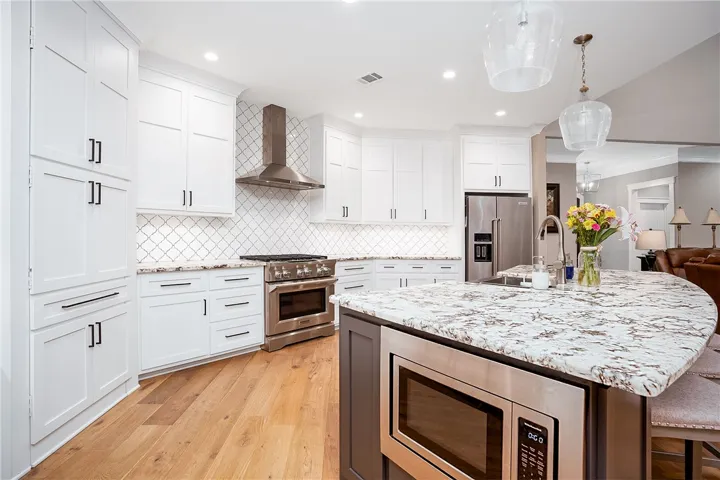 A well-appointed kitchen features a large curved island, stainless appliances, and warm wood flooring.