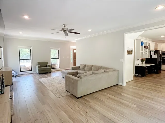 This airy living space features warm flooring, crown molding, and an open layout to the kitchen.