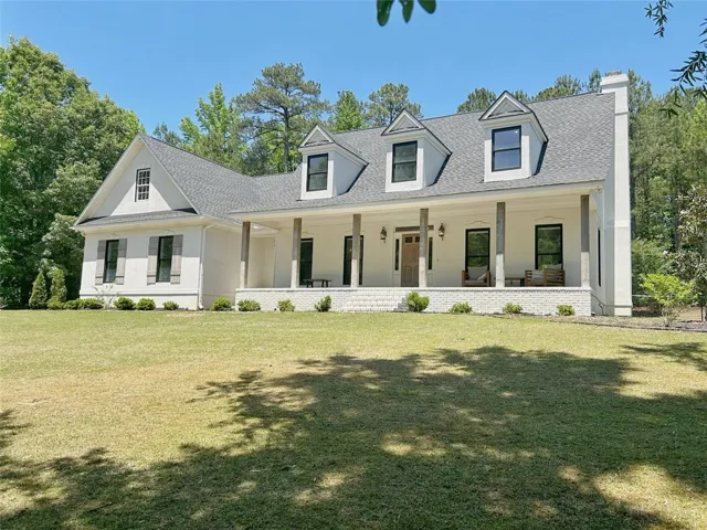 This charming home offers a welcoming facade with a covered porch, set against a backdrop of lush greenery.