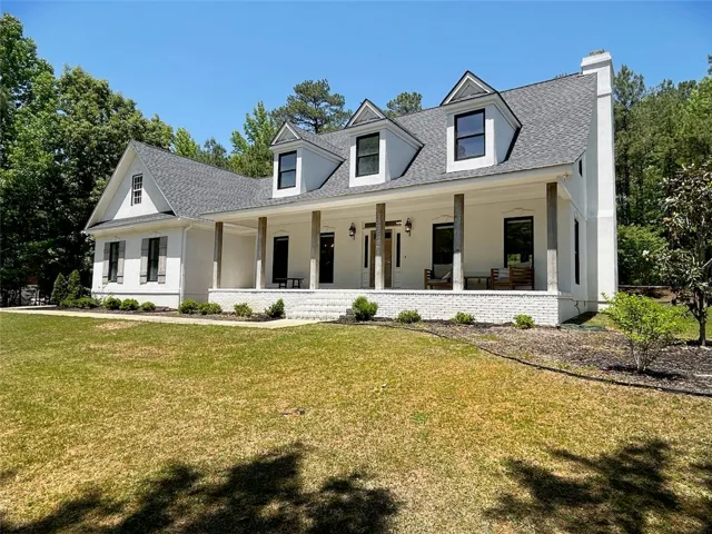 This classic white residence offers a welcoming facade with a charming porch and lush green surroundings.