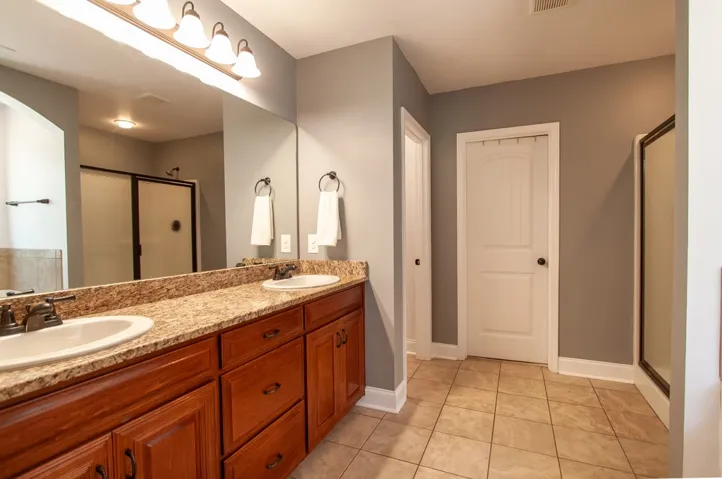 This spacious bathroom features a double vanity and sleek tile flooring.
