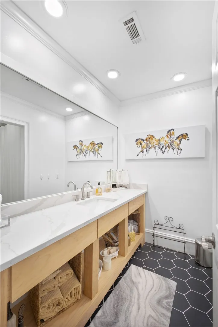 This bright bathroom offers a dual vanity with a large mirror and sleek hexagonal flooring.