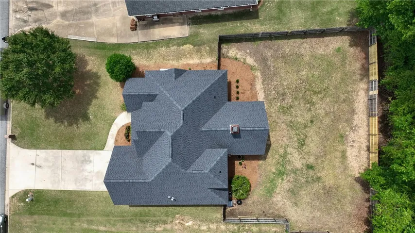 An aerial view showcases a residential property featuring a dark shingle roof and expansive yard.