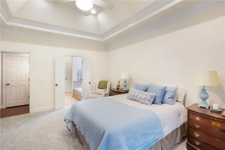 This tranquil primary bedroom features an elegant tray ceiling and soft carpeting.