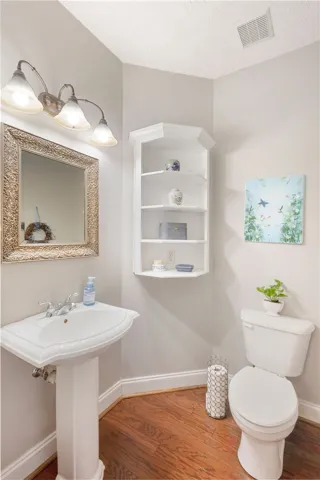 This bright bathroom features warm wood flooring and a classic pedestal sink, offering functional elegance.