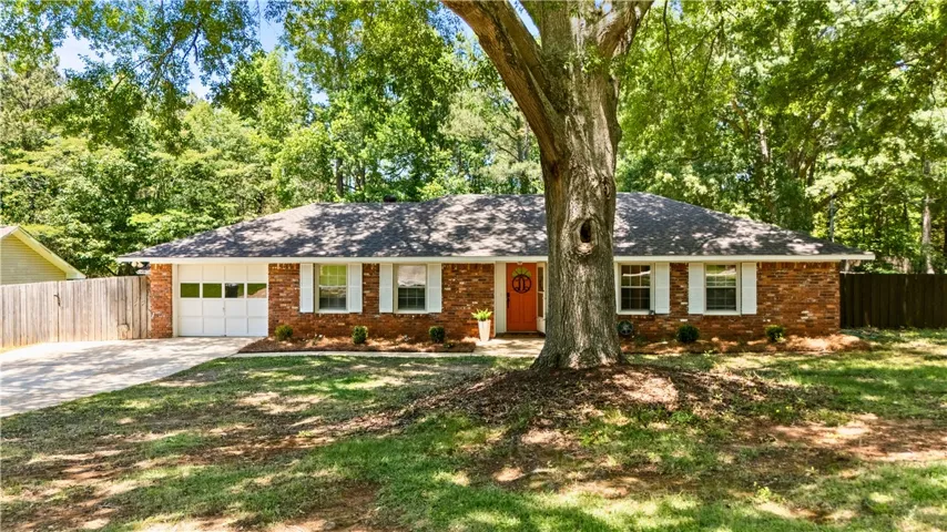 This charming brick home features a spacious driveway and lush green surroundings.
