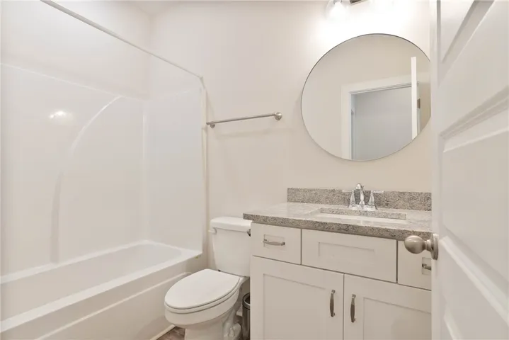 This bathroom features a contemporary vanity with a granite countertop and a sleek round mirror.