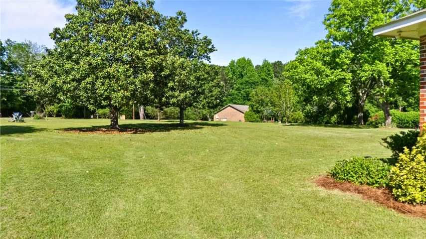 Expansive flat green yard with mature trees offers serene outdoor living.