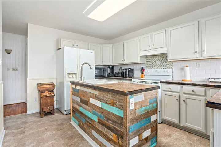 A rustic-chic kitchen features a charming island with reclaimed wood, complemented by crisp white cabinetry and a tiled backsplash.