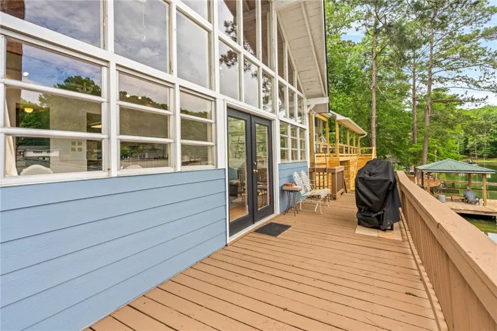 A spacious wooden deck extends from a home with large windows, overlooking a serene waterfront with a covered dock.