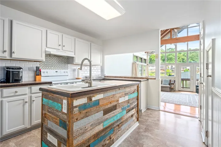 A spacious kitchen featuring a vibrant reclaimed wood island, connecting seamlessly to a sunlit living area with generous windows.
