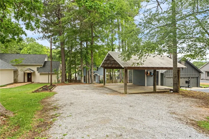 A spacious gravel driveway provides ample parking next to a convenient carport and detached garage structures.