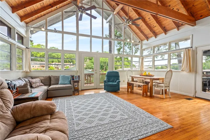 A vaulted wood-beamed ceiling crowns this sun-drenched living space, offering panoramic views through floor-to-ceiling windows and French doors.