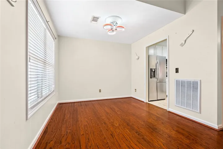 Rich hardwood flooring extends throughout this versatile space, featuring a large window with privacy blinds.