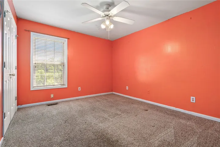 This cozy bedroom offers carpet flooring, a window with blinds, and a ceiling fan for comfort.
