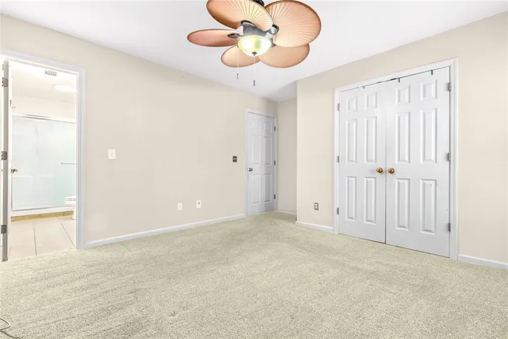 A well-lit bedroom features plush carpeting, a tropical ceiling fan, and convenient closet access.