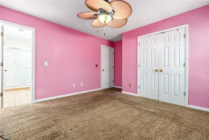 This spacious bedroom features a ceiling fan, plush carpet, and convenient access to an en-suite bathroom.