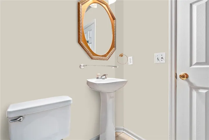 A well-appointed powder room with a sleek pedestal sink and golden framed mirror.