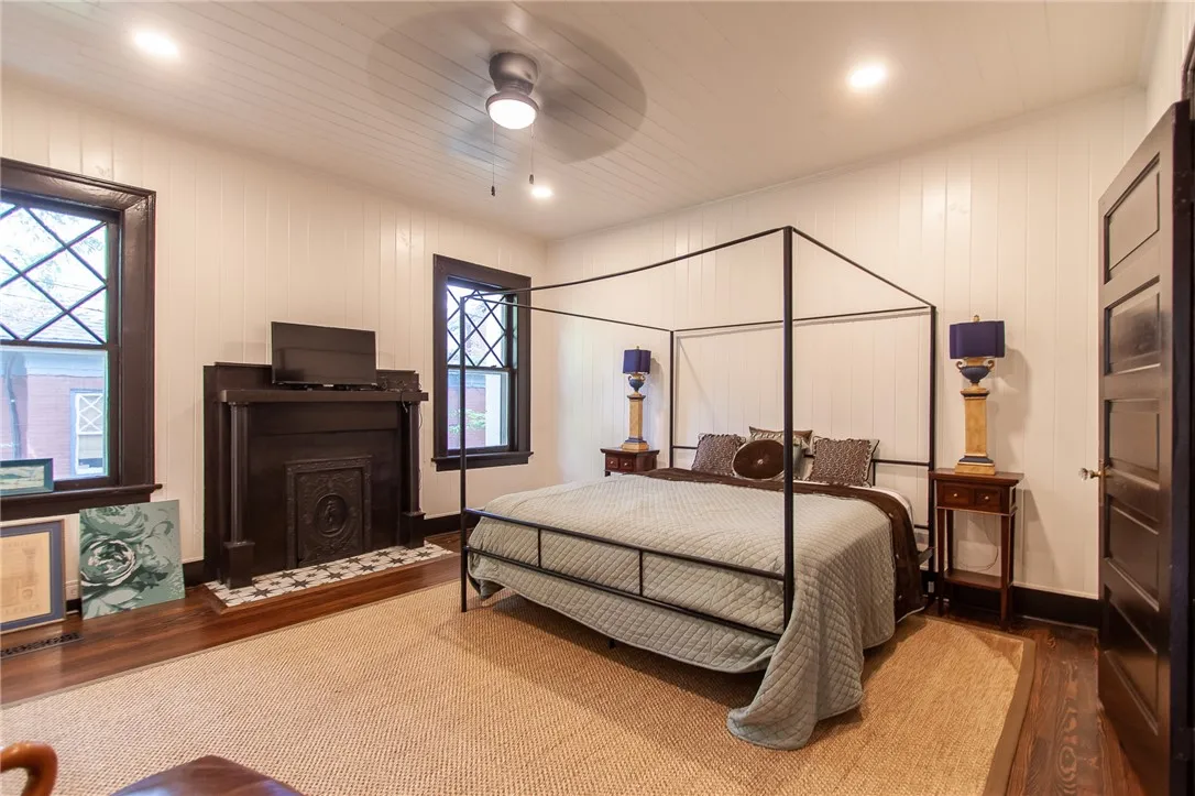 This inviting bedroom features a cozy fireplace, natural light, and classic architectural details.