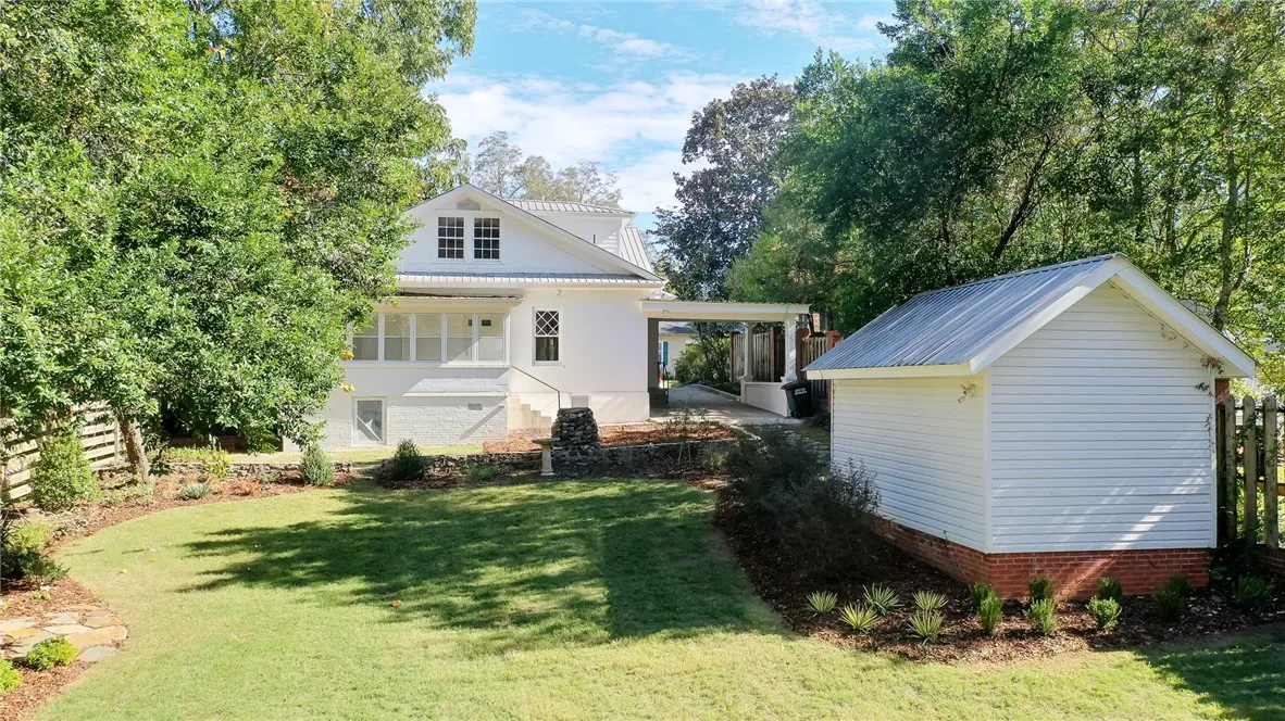 This classic white home features a lush green yard and a charming detached outbuilding.
