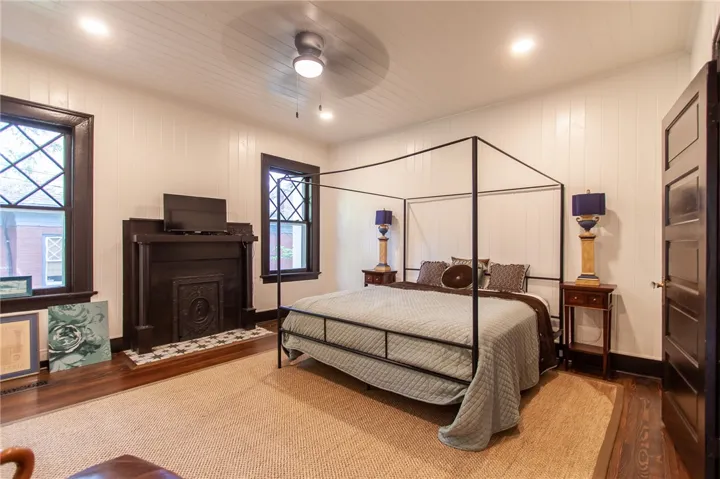 This inviting bedroom features a cozy fireplace, natural light, and classic architectural details.