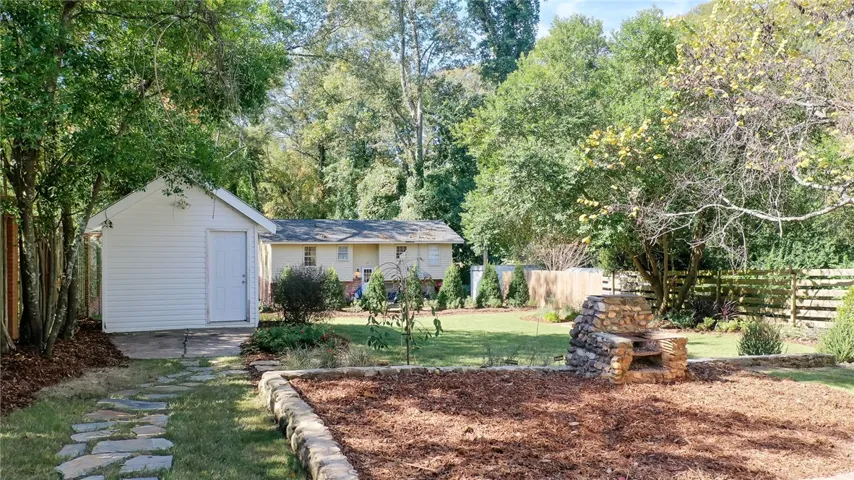This verdant backyard features a charming shed, stone pathway, and an inviting outdoor fireplace.