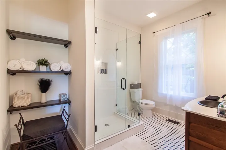 This bright bathroom features a spacious glass-enclosed shower and practical open shelving.