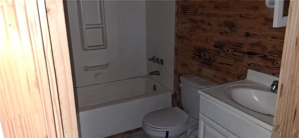 This bathroom features a simple bathtub, toilet, and vanity against rustic wood-paneled and classic white walls.