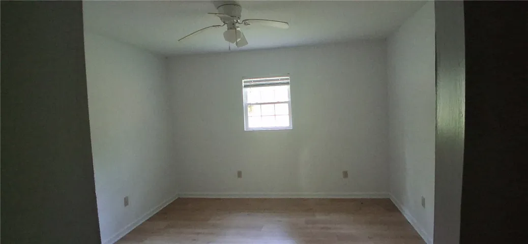 A well-lit bedroom featuring light wood flooring and a central window for natural illumination.