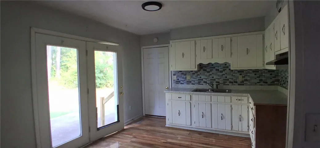 This kitchen area features ample white cabinetry, a tiled backsplash, and direct outdoor access through glass panel doors.