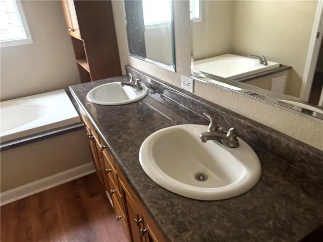 This primary bathroom features a dual vanity, a built-in tub, and warm wood flooring.