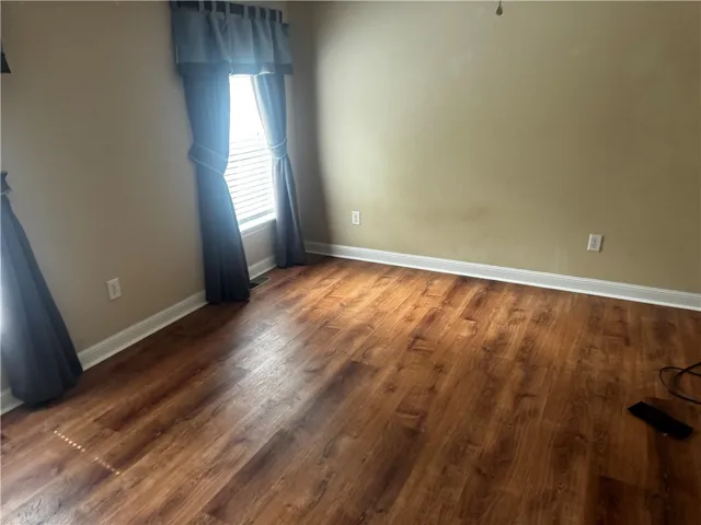 This versatile room features warm wood flooring and a window dressed with tasteful drapes.