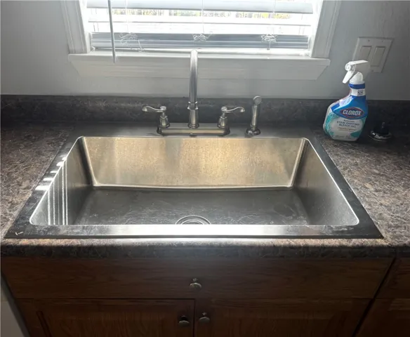 A deep stainless steel sink is set into a marbled countertop beneath a bright window.