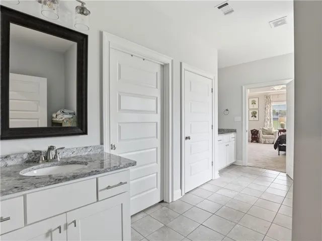 Granite counters and tile flooring highlight this well-appointed bath, leading to a plush bedroom.