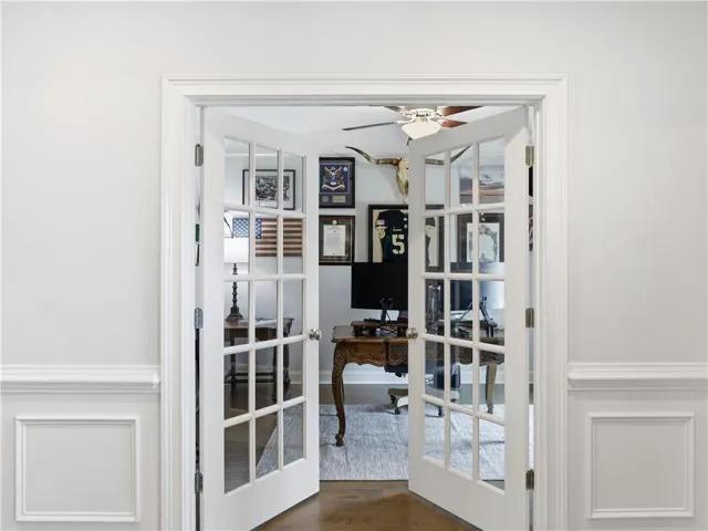 French doors open into a bright home office featuring elegant crown molding and rich hardwood flooring.