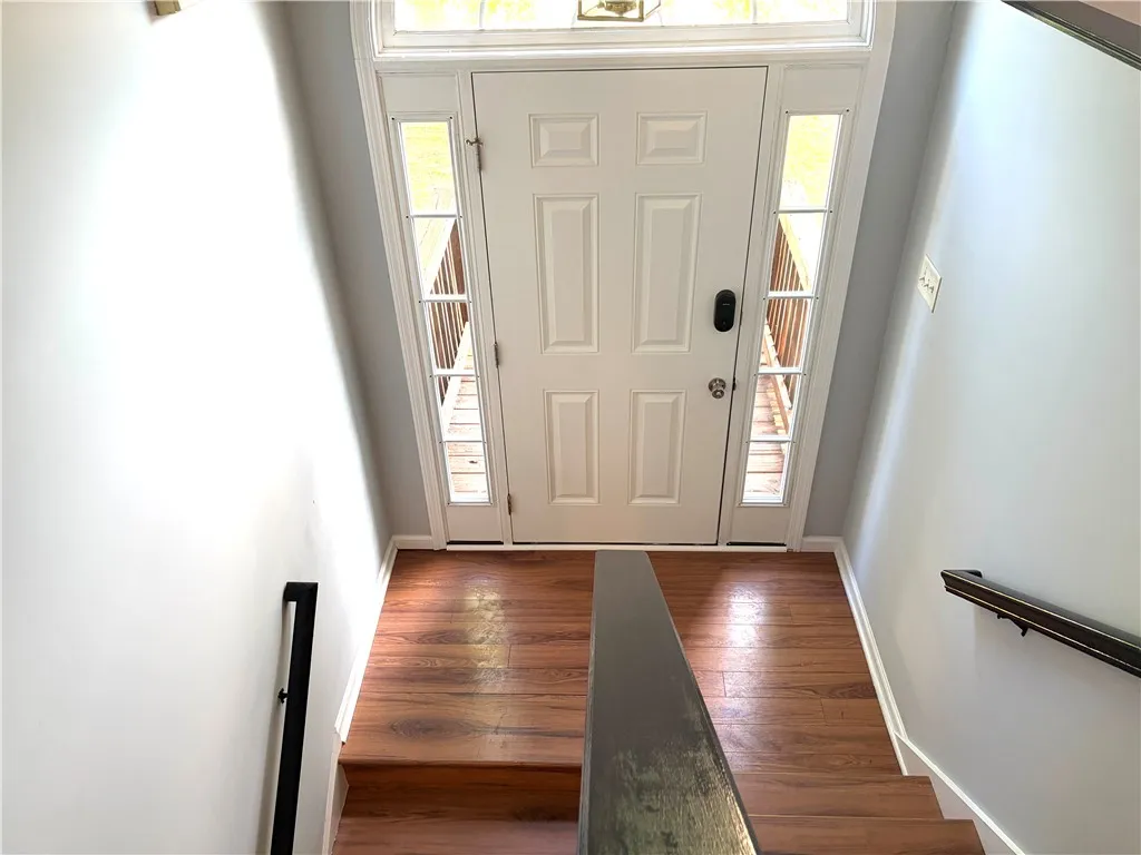 A welcoming entryway with rich wood flooring leads to a paneled front door flanked by sidelight windows.