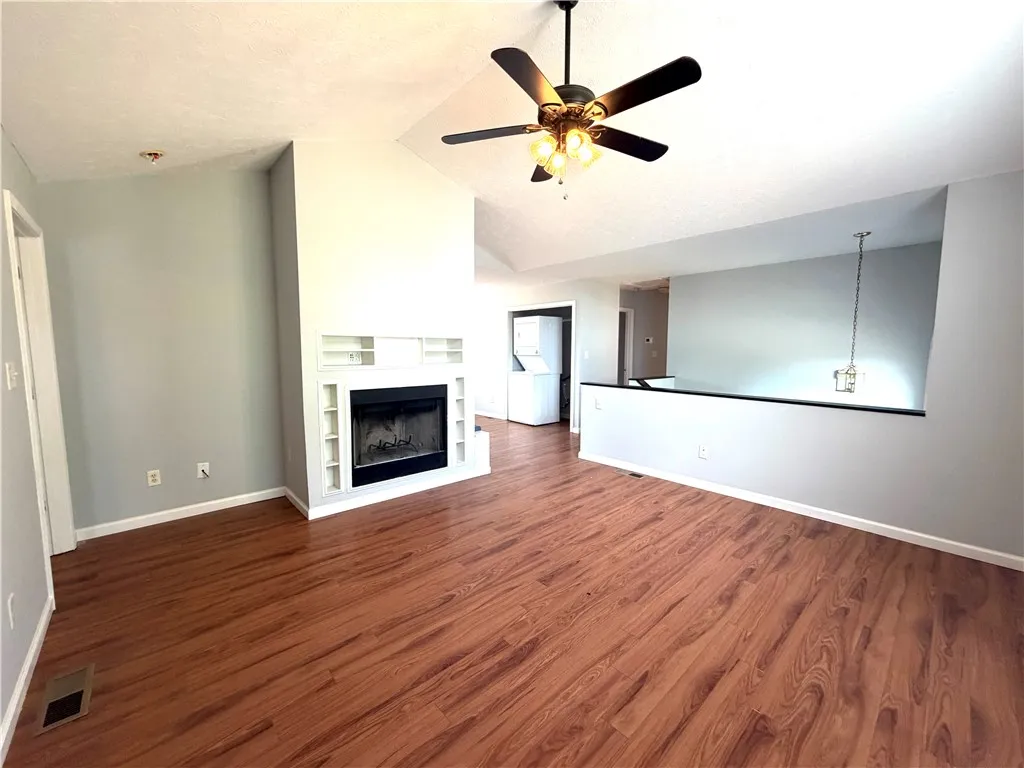 This inviting living space features vaulted ceilings, a cozy fireplace with built-in shelving, and warm wood flooring.