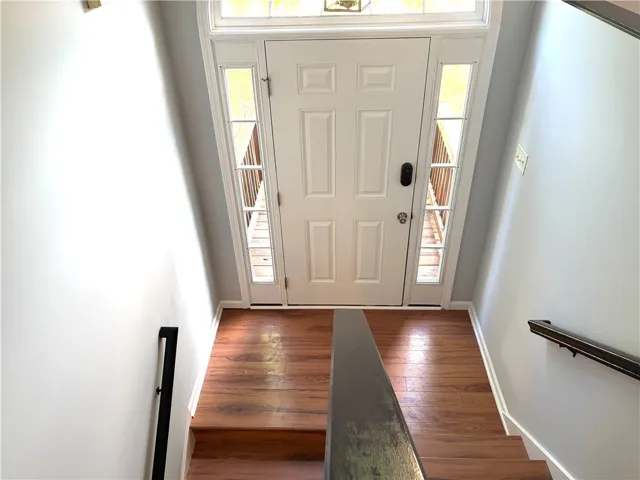 A welcoming entryway with rich wood flooring leads to a paneled front door flanked by sidelight windows.