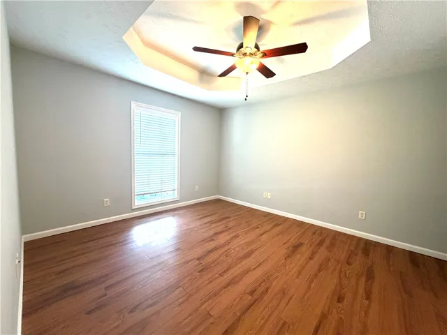 This naturally illuminated bedroom boasts a tray ceiling and warm wood flooring.